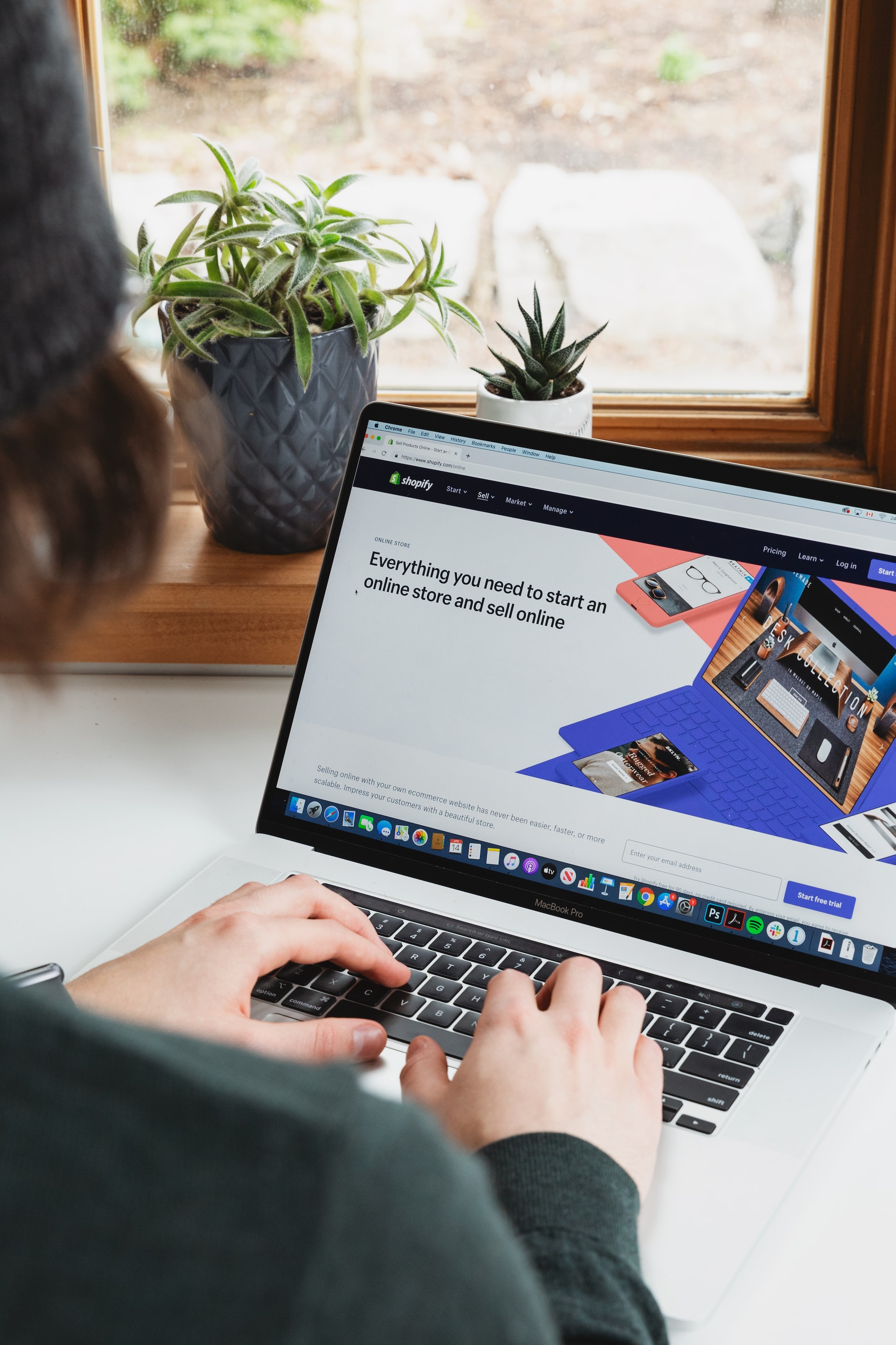 Person typing on a laptop. The laptop screen shows the Shopify homepage 